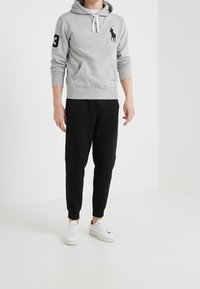 Sudadera gris con logo de polo negro y número 3 en la manga, combinada con pantalones jogger negros y zapatillas blancas sobre un fondo neutro.