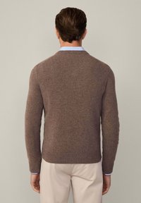 Brauner Rundhalsausschnitt-Pullover aus weichem Material, mit gerippten Bündchen und Saum. Über einem hellblauen Hemd mit Kragen getragen, von hinten betrachtet.