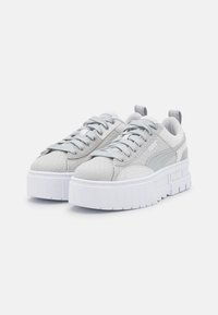 Sneaker grigie chiare con parte superiore testurizzata, lacci piatti e una spessa suola in piattaforma bianca. Presentano un logo di lato e un manico sul tallone.