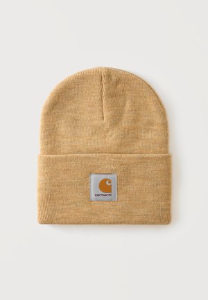 Bonnet en maille marron clair avec bord-côte replié et écusson carré au centre devant affichant le nom de la marque Carhartt.