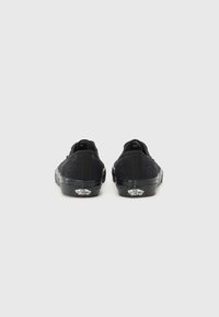Black lace-up sneakers with textured fabric, rubber soles, and contrasting logo detail at the back. Minimalist design with no embellishments.