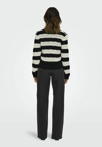 Pull en tricot rayé noir et blanc avec un motif texturé, des poignets et un ourlet côtelés. Associé à un pantalon taille haute gris foncé.