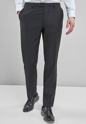 Pantalones de vestir negros, hechos de una tela suave, con un ajuste entallado, lazos para cinturón y cierre de botón. Combinados con zapatos de cuero oscuros.