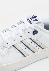 Vita lädersneaker med tre marinblå och beige ränder, texturerade mockadetaljer, vita snören och en logotyppräglad tunga.