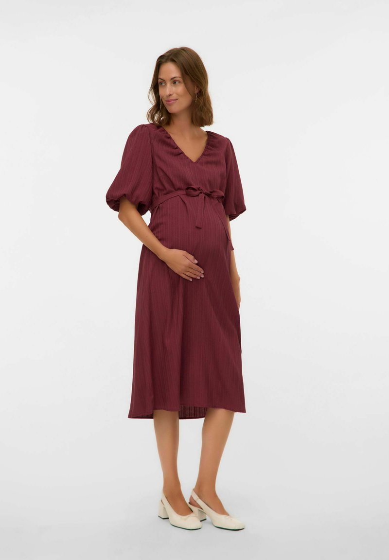 Vestido de maternidad en burdeos oscuro con escote en V, mangas cortas abullonadas y una cintura con lazo. Tejido ligero con una sutil textura acanalada.