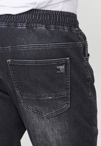 Joggers de denim negro con una cinturilla elástica, bolsillo trasero, costuras en contraste y un acabado sutilmente desgastado.