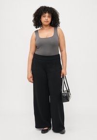 Grå bodysuit med firkantet hals, kombinert med svarte vide bukser. Modellen holder en liten svart håndveske og har på seg svarte leiligheter med pynt.