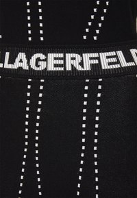 Black fabric with white striped pattern and small rectangles. Features a prominent black and white logo band at the waist.