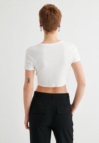 Camiseta blanca corta de manga corta, combinada con pantalones negros de tiro alto que cuentan con dos bolsillos traseros. Tejido suave y ligero.
