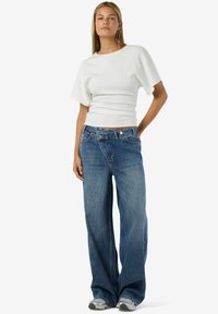 Balts ribots īss piedurkņu tops kombinēts ar vaļīgām gaisīgi zilām džinsa biksēm. Džinsiem ir klasiskas piecu kabatu detaļas un viegla izbalēšana.