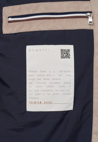 Navy fabric featuring a beige suede panel with a horizontal zip pocket, label detailing "Premium Suede," and a QR code for information.