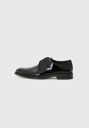 Scarpa da uomo in pelle nera lucida, con finitura in vernice, punta arrotondata e cuciture esterne. Presenta un tacco basso e chiusura con lacci.