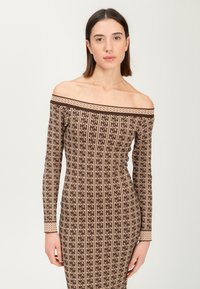 Frau mit glattem braunen Haar trägt ein eng anliegendes, schulterfreies langärmliges Kleid mit braunem Muster auf einem schlichten Hintergrund.