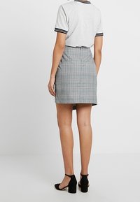 Grijze geruite rok met een hoge taille, ontworpen met een rechte snit en subtiele textuur. Gecombineerd met een lichtgrijze, geribbelde T-shirt met korte mouwen.