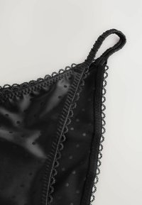 Lencería de satén negro con un patrón de lunares, borde de encaje en los bordes y tirantes ajustables para un mejor ajuste. Textura suave, detalles de diseño delicados.