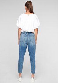 Light blue high-waisted denim jeans with a tapered leg and subtle fading, paired with a white puff-sleeve blouse and silver sneakers.
