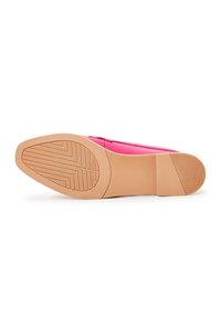 Semelle d'une chaussure plate rose montrant une adhérence en caoutchouc texturé sur les zones des orteils et du talon, avec une semelle intermédiaire lisse et un talon bas.