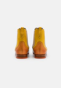 Botas de tornozelo amarelas em pele com um painel em tecido bege, realces em castanho e costura decorativa. Sola plana e alça de puxar na parte de trás.