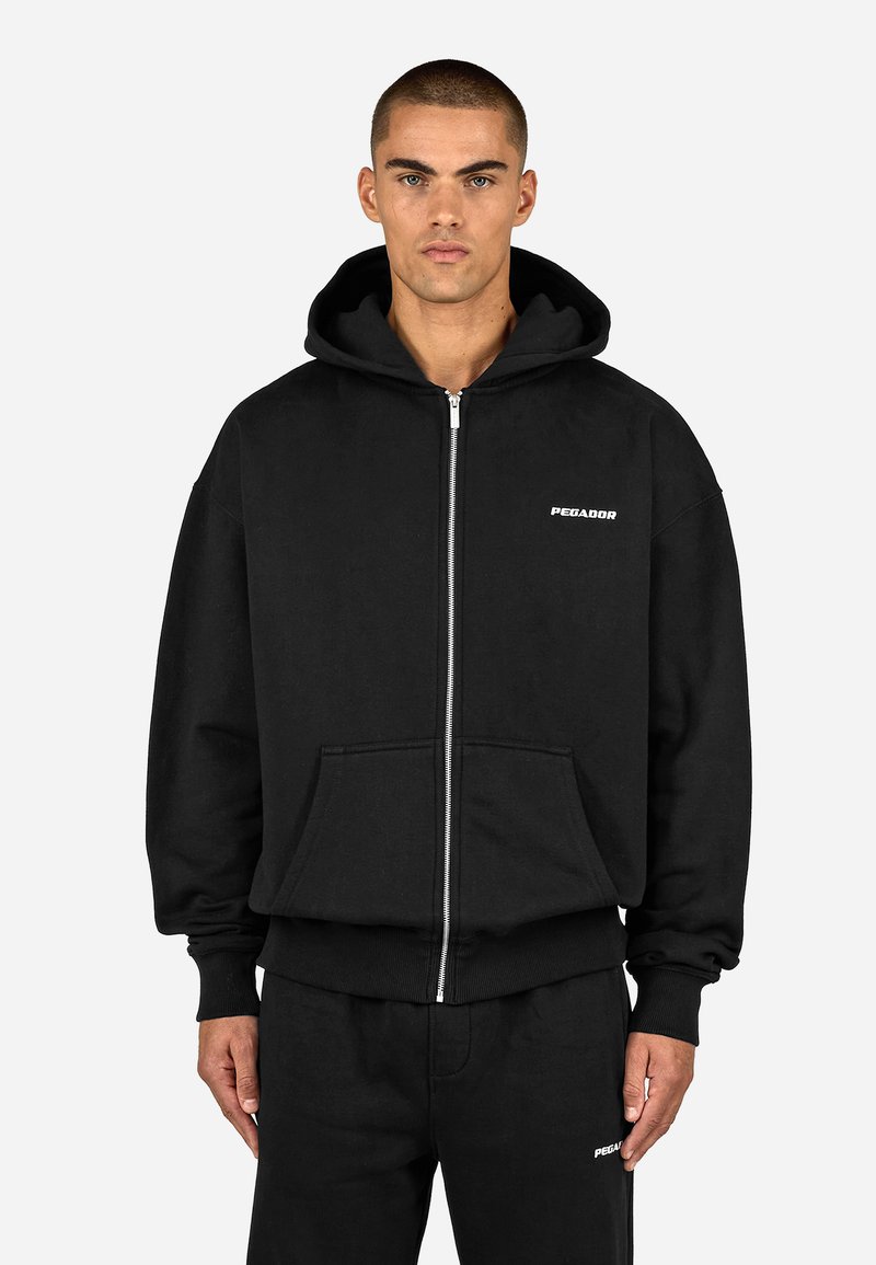 Sweatshirt preta com fecho de correr, feita de algodão, com bolso frontal, apresentando um logótipo branco simples no lado esquerdo do peito e punhos e bainha canelados.