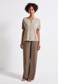 Helle beige kurzärmlige Hemd mit Knopfleiste, kombiniert mit lockeren, hellbraunen Leinenhosen. Einfacher, legerer Schnitt und weiche Textur.