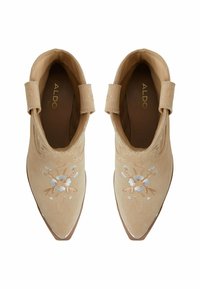 Botas de tobillo de ante beige con punta afilada, que presentan bordados florales en azul claro y marrón, y correas alrededor del tobillo para un ajuste seguro.