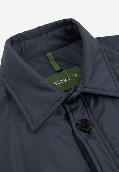 Granatowa ocieplana kurtka z wyłogami, czarnymi guzikami i zieloną metką z napisem "SLOWEAR". Gładki, lekki materiał z delikatnym połyskiem.