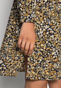 Abito floreale con base blu navy, caratterizzato da fiori gialli, bianchi e azzurri. Maniche lunghe e dettaglio con spacco laterale. Tessuto morbido.