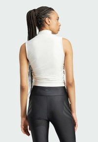 Witte mouwloze crop top met een hoge hals, voorzien van een gladde textuur, gecombineerd met zwarte high-waisted leggings met subtiele merktekens.