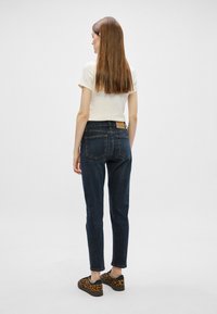 Ciemnoniebieskie dżinsy o slim fit i zwężanych nogawkach. Połączone z kremowym t-shirtem i trampkami w panterkę. Prosty wzór tylnej kieszeni.