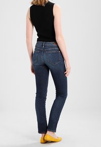 Tmavě modré skinny džíny s hladkým denimovým texturem, se zadními kapsami a hnědou koženou nášivkou. V kombinaci se žlutými balerínami.