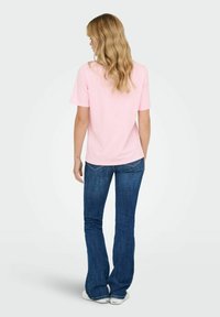 Lichtroze katoenen t-shirt met korte mouwen, gecombineerd met donkerblauwe wijde spijkerbroeken, gedragen door een persoon die van achteren is gezien. Glad oppervlak.