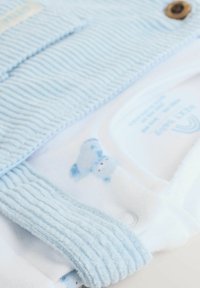 Világoskék bordás anyag, texturált mintázattal, patenttal záródik, és egy fehér body, amelyen kék plüssmaci mintázat található.