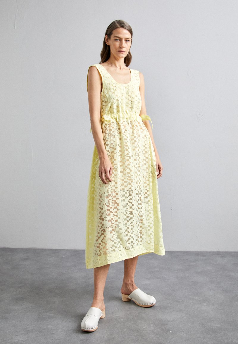 Robe en dentelle jaune avec un décolleté arrondi, un lien en ruban à la taille et une coupe fluide. Présente des motifs texturés, un design superposé et une longueur jusqu'aux chevilles.