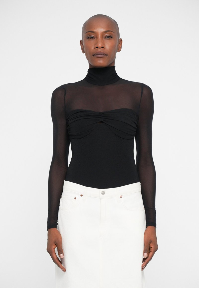 Langærmet sort bodysuit med høj hals og samlet frontdetalje, parret med en hvid denimnederdel med lukning foran.