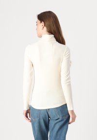 Langermet genser med høy hals i elfenbensfarget ribbestrikket stoff, med en tettsittende design og minimale sømdetaljer, kombinert med blå denimjeans.