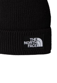 Căciulă tricotată neagră, cu un design cu nervuri, având o etichetă albă cu marca "The North Face" pe față.
