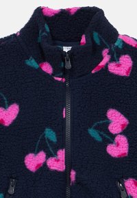 Mornarska flis jakna s uzorcima ružičastog srca i tirkiznim listovima, visokim ovratnikom i crnim detaljima na patent zatvaraču. Mekana tekstura i udoban dizajn.
