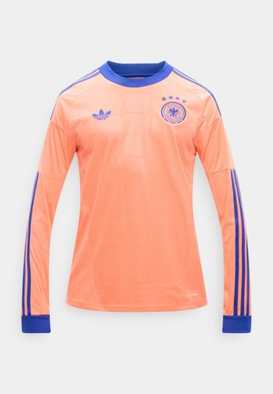 Dres za nogomet dugih rukava u breskvastoj boji s plavim ovratnikom i manžetama, plave Adidas pruge na rukavima te logom njemačke reprezentacije s četiri zvjezdice.