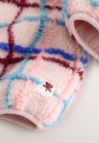 Blødt pink fleece-stof med ternet mønster i blå, rød og lyserøde accenter. Har afrundede ærmer og en lille logo-etiket.