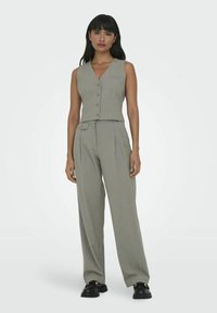 Grå ærmeløs vest med knaplukning og matchende højtsiddende bukser med plisseringer, parret med kraftige sorte sko.