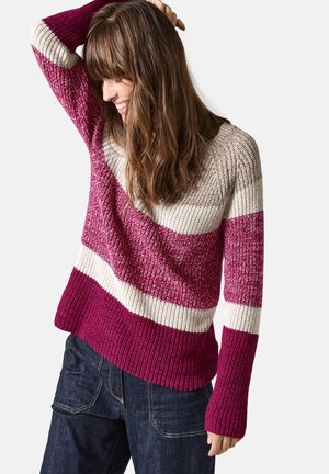 Pull en laine avec des rayures horizontales en rose foncé, rose clair et crème. Présente un large col et des poignets côtelés, associé à un jean sombre.