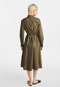 Oliwkowa sukienka z lekkiej tkaniny, z kołnierzykiem, długimi rękawami i elastyczną talią. Projekt ma długość do połowy łydki i lekki, zwiewny kształt.