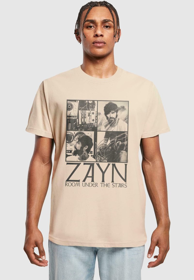 Krémové bavlněné tričko s grafickým designem obsahujícím čtyři monochromatické obrázky a text "ZAYN ROOM UNDER THE STAIRS" napsaný tučným písmem.