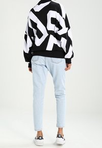 Schwarzweißes übergroßes Sweatshirt mit grafischem Design, kombiniert mit hellblauen Jeans und schwarzen Sneakern mit weißen Akzenten.