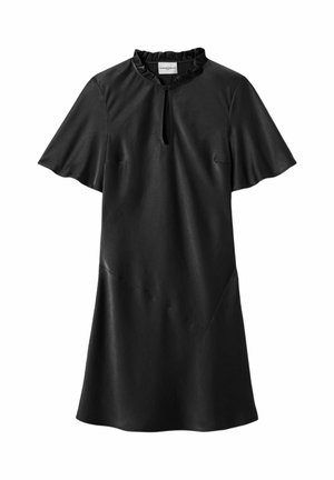 Femme portant une robe noire sans manches, une chemise ample rayée jaune avec des poignets et un col blancs, des sandales noires à brides, tenant une pochette noire.