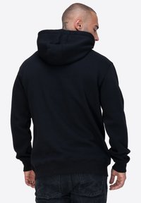 Felpa nera con cappuccio, polsini e orlo a costine, texture morbida, vestibilità casual, design semplice senza motivi o loghi visibili.