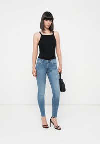 Fekete ujjatlan bodyszután világoskék skinny farmerral párosítva. Az öltözéket fekete pántos magassarkú cipő és egy kis fekete kézitáska egészíti ki.