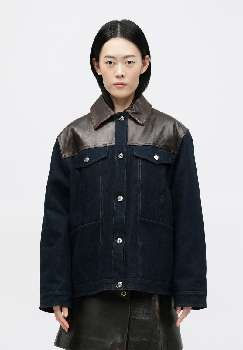 Ναυτικό μπλε μπουφάν με καφέ δερμάτινες λεπτομέρειες στ�ους ώμους, ασημένια κουμπιά, δύο εμπρόσθιες τσέπες και κλασικό σχέδιο γιακά.