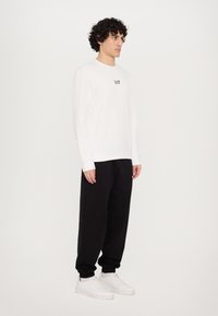Hvid langærmet sweatshirt med logo på brystet, parret med sorte tapered sweatpants og hvide sneakers. En simpel, afslappet påklædning.