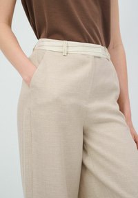 Beige linnen broeken met een getailleerde pasvorm, voorzien van een platte voorkant, zijzakken en een lichtgekleurde riem met subtiele strepen.
